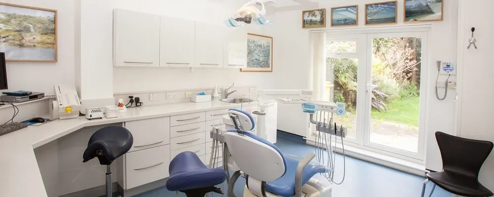 Salle de soins d’un cabinet dentaire avec fauteuil, plan de travail et fenêtre sur jardin : nettoyage d’un cabinet dentaire